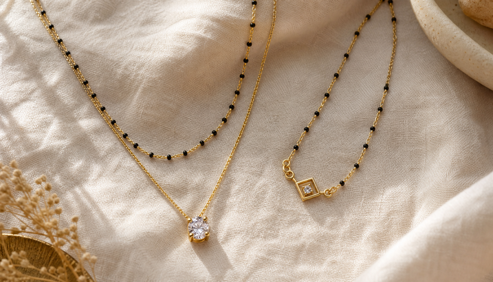 Two gold mangalsutras on a soft linen surface, one statement solitaire layered design and one minimalist fine chain with small geometric pendant and black beads, warm natural light, photorealistic, no text